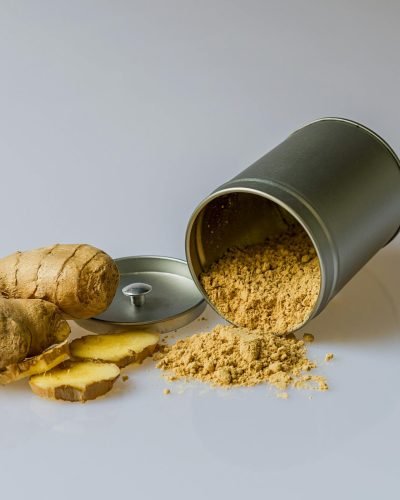 Close-up of fresh ginger root with sliced pieces and ginger powder spilled from a metal container.